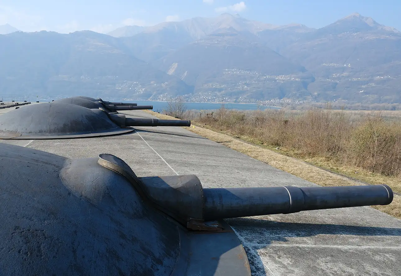 Eine Betonmauer, geschmückt mit einer beträchtlichen Anzahl von Kanonen, mit Blick auf den See und die Berge im Hintergrund