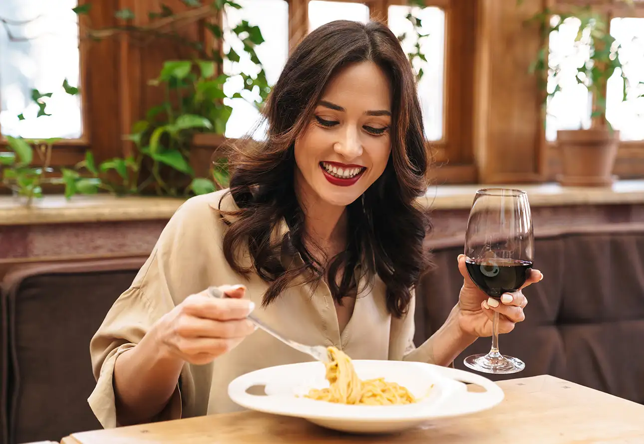 a woman is eating pasta and drinking wine