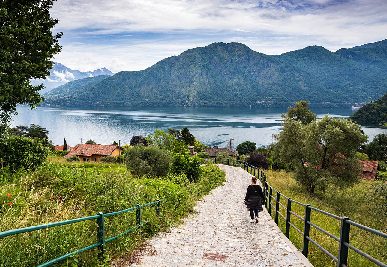 An individual casually strolling along enchanting Greenway of Lake Como overlooking a lake with mountain views